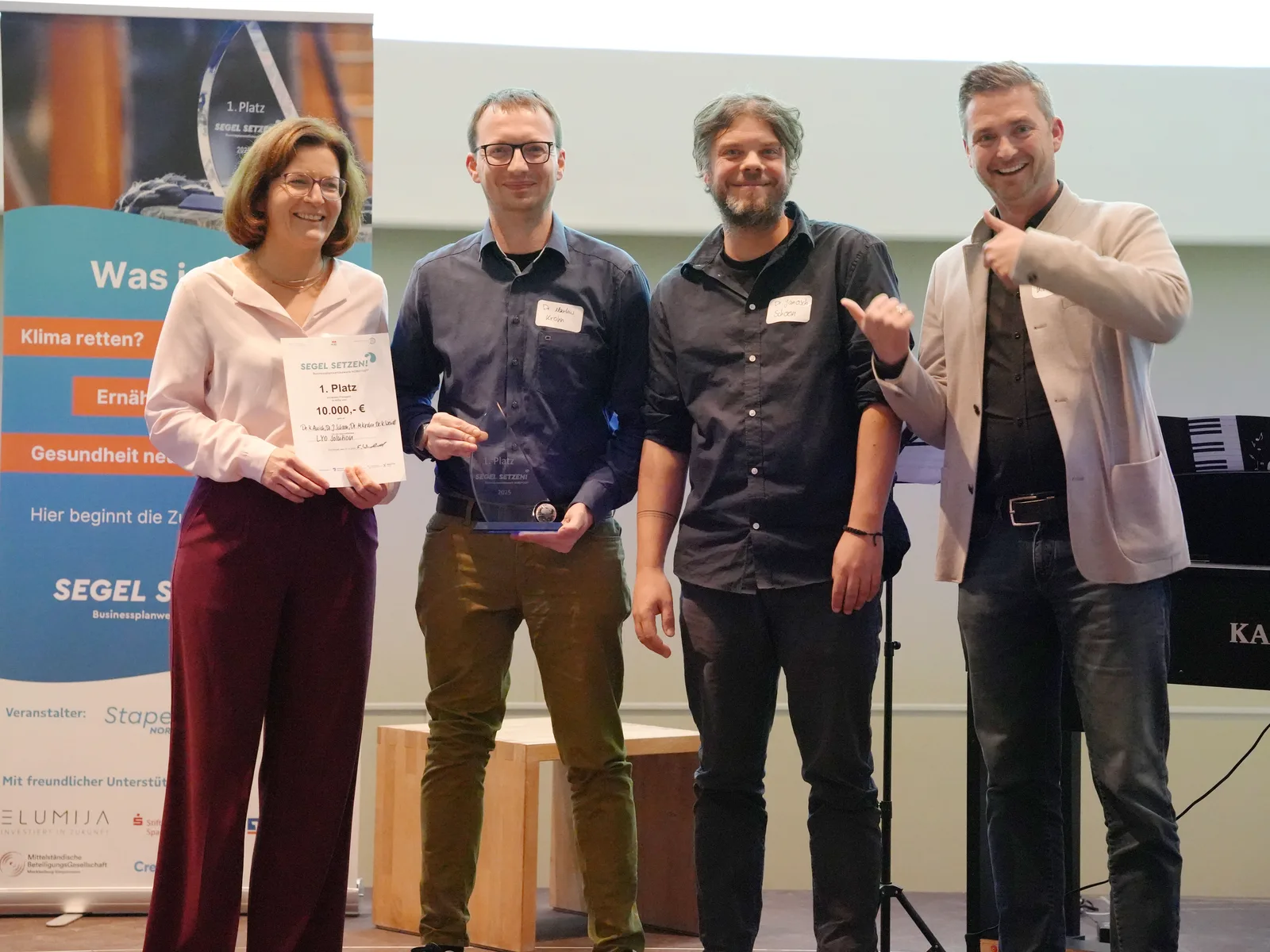 Preisträgerteam LYOSolution des Businessplanwettbewerb MV 2025 auf der Bühne mit Urkunde für den 1. Platz und Glaspokal.